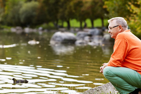 Mature Man Crouching Near Pond