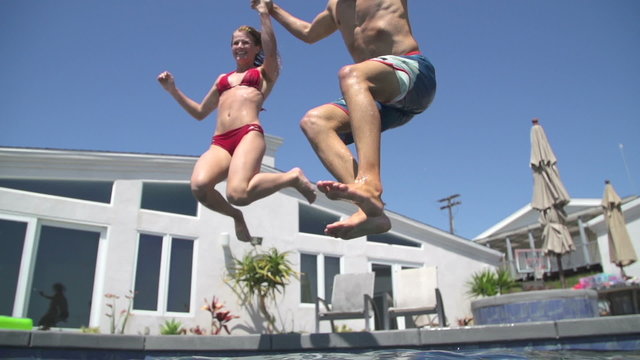 Young Happy Couple Holding Hands Running And Jumping Into Pool