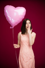 Young woman holding heart shaped balloon and yawning