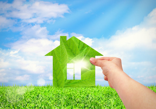 Hand Holding Green House With Field And Blue Sky Background.