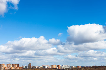 white clouds in blue spring sky over city