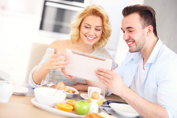 Obraz na płótnie Canvas Happy couple eating breakfast and using tablet