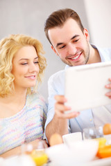 Happy couple eating breakfast and using tablet