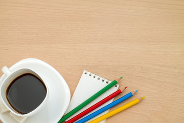 Цветные карандаши, кружка кофе,блокнот, на столе