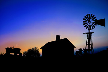 Silhouette of a farm tractor, house and windmill.