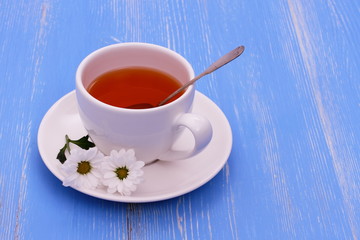 White tea cup and flowers on blue wooden horizontal