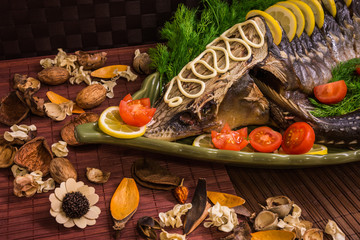 Sturgeon decorated with lemon and tomatoes on a green plate