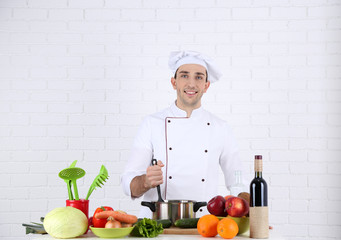 Chef at table with different products and utensil in kitchen on white wall background