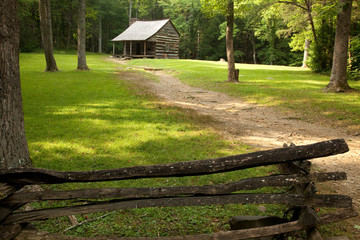 Old log farmhouse with a dirt path and fence