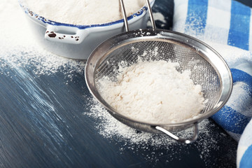Sifting flour through sieve on wooden table, closeup