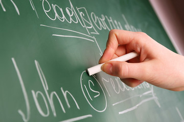 Teacher hand writing grammar sentences on blackboard background