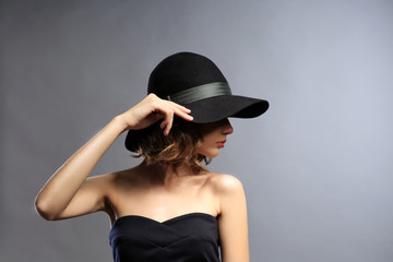 Fototapeta na wymiar Portrait of beautiful model in black dress and hat on gray background