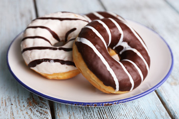 Delicious donuts with icing on plate on wooden background