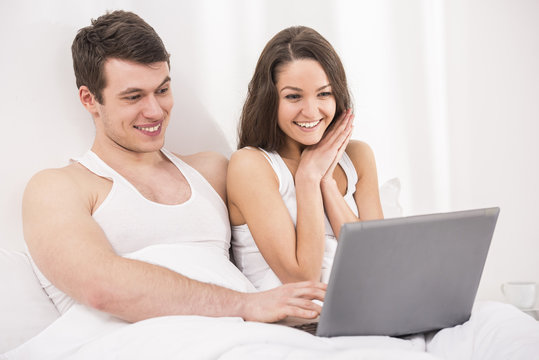 Smiling young couple using leptop in bed.