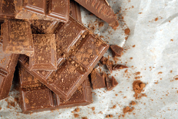 Pieces of chocolate with cocoa on parchment, closeup