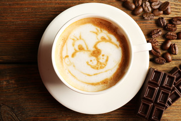 Cup of coffee latte art with grains and chocolate on wooden table, top view