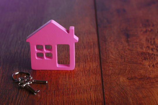 Toy house with key on wooden background