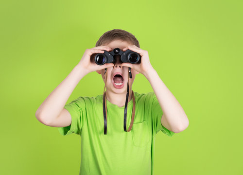 Surprised young boy with binoculars on green background.