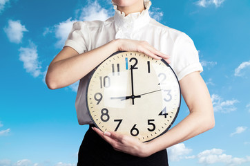 Business woman holding a clock on the sky backround