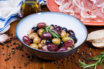 Olives in bow with prosciutto on wooden table