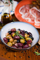 Olives in bow with prosciutto on wooden table