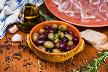 Olives in bow with prosciutto on wooden table