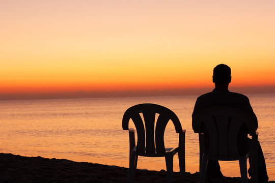Man sits on chair alone in sunset