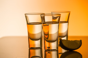 Tequila shot with a slice of lime on the glass orange background