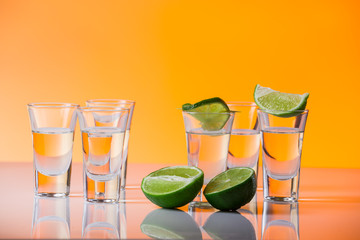 Tequila shot with a slice of lime on the glass orange background