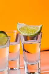 Tequila shot with a slice of lime on the glass orange background