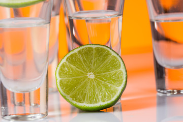 Tequila shot with a slice of lime on the glass orange background