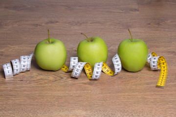 three green apples and measure tape on table
