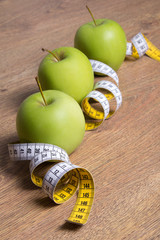 close up of three green apples and measure tape on table