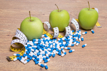 diet concept - apples, pills and measure tape on table