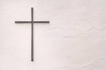 Kreuz aus Metall an einer weissen Wand