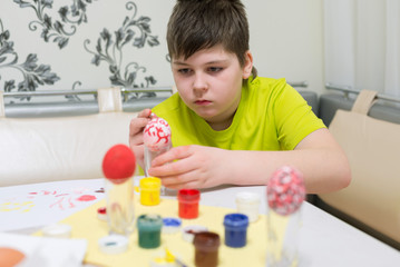 Obraz na płótnie Canvas boy paints the Easter eggs with a brush