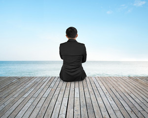 Rear view businessman sitting on wooden floor with sky sea