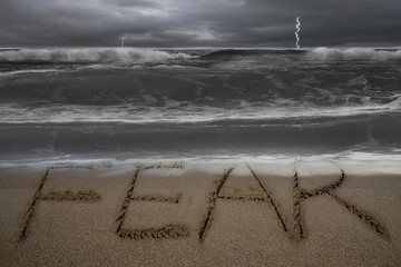 Fear word hand written on sand beach with stormy ocean