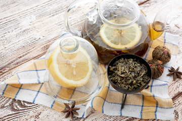 Ripe lemon, cinnamon and fruit drink in glass teapot on wooden