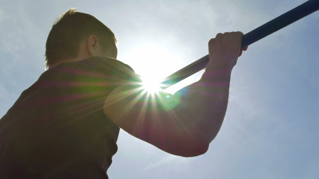 Man pull on the horizontal bar with bright sun background