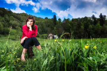 Elegant woman sitting on suitcase in the middle of a meadow