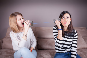 Blonde and brunette women talking with tin can telephone