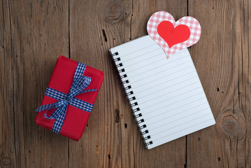 Notebook with gift and hearts on old wooden background