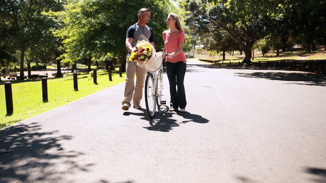 Happy couple walking with bike and bunch of flowers