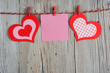 Paper hearts and blank note on old wooden background
