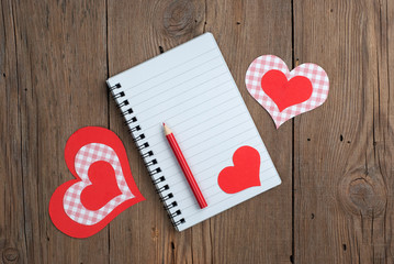 Notebook with hearts and pencil on old wooden background