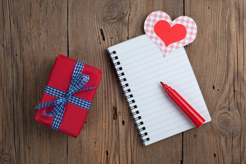 Notebook with gift, felt pen and hearts on old wooden table