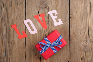 Gift and paper letters forming word LOVE on old wooden table