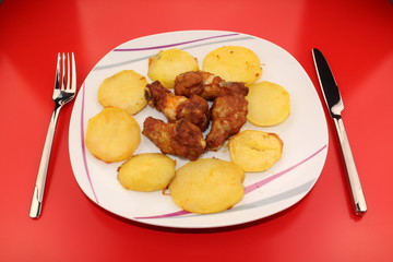 Baked and sauced chicken drumsticks surrounded by potatoes