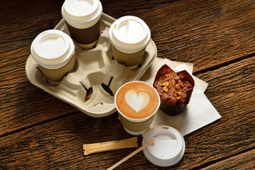 Paper cups of coffee latte and cake on wooden background